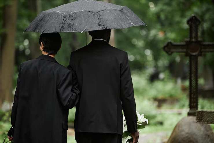 multiethnic-couple-black-suits-walking-umbrella-cemetery